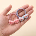 Two pairs of heart bow hair ties held in a hand to show their small size