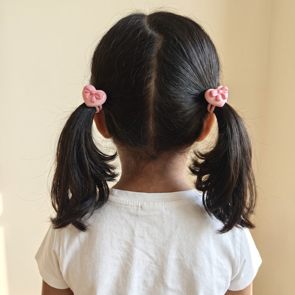 Girl wearing pink heart bow hair ties in two pigtails, back view
