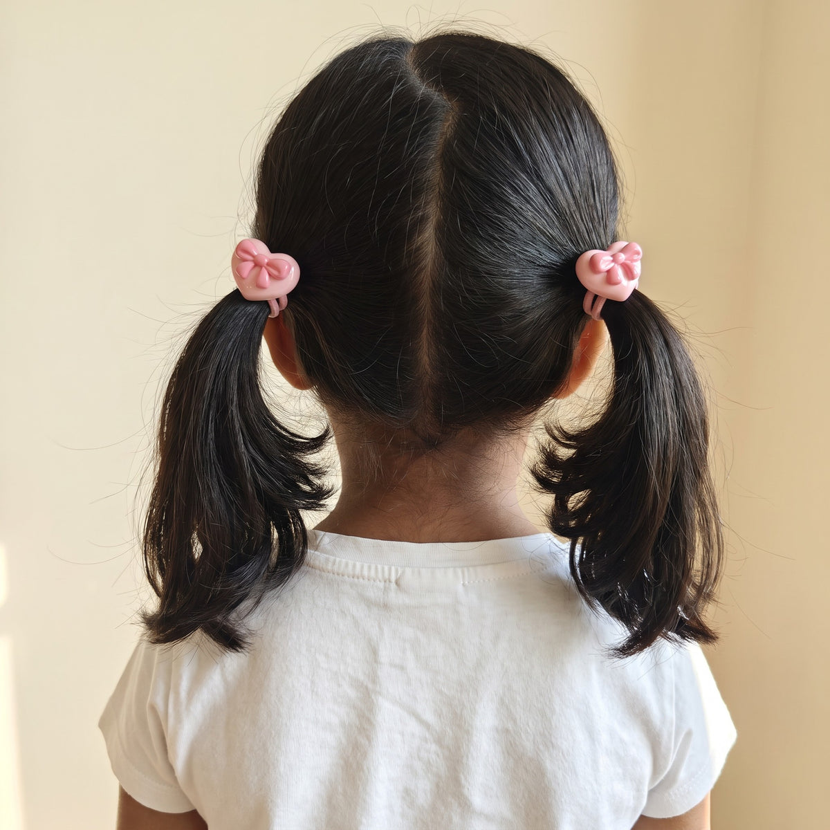 Girl wearing pink heart bow hair ties in two pigtails, back view