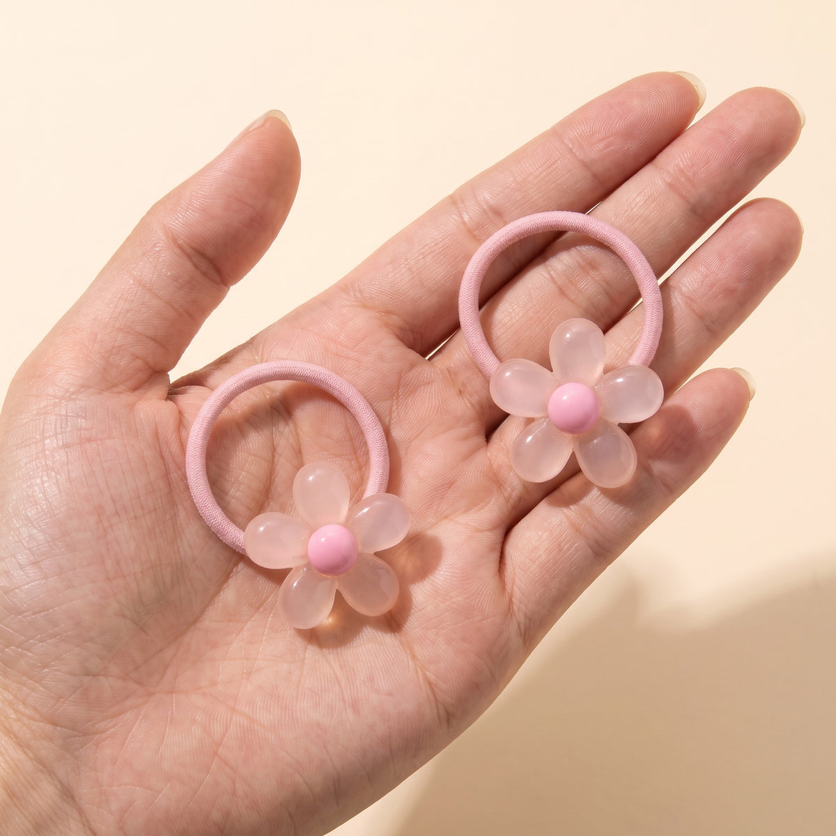 A pair of blush jelly daisy hair ties on an open hand to show size